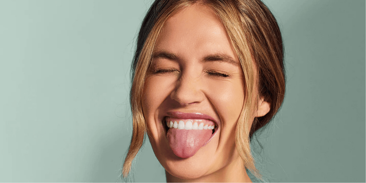 Smiling woman showing her teeth and tongue against a light green background.