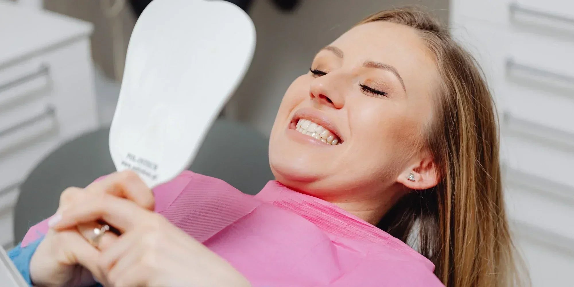 A patient at the dentist smiling in the mirror at her teeth from before and after thanks to xylitol toothpaste