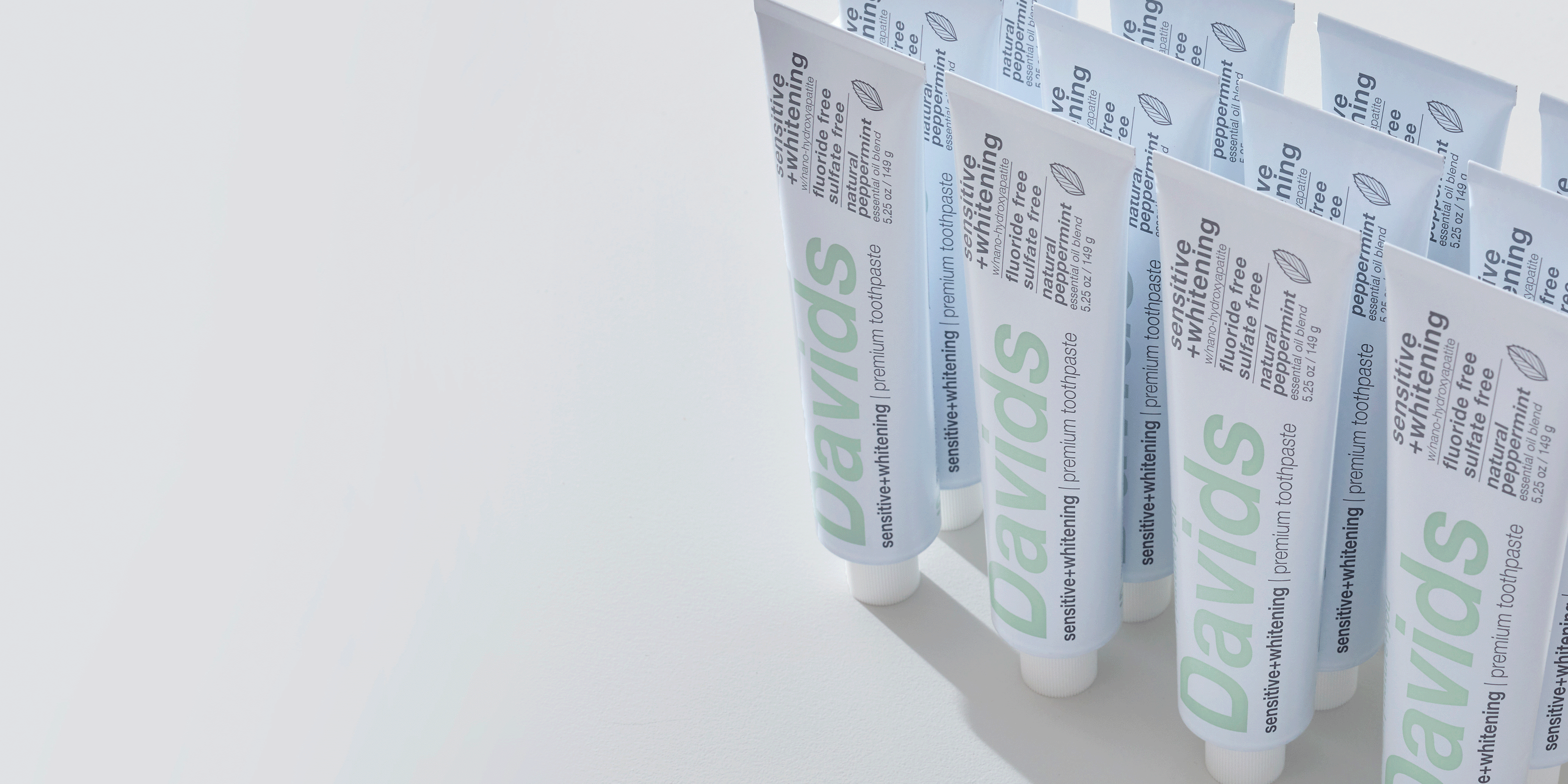 Rows of Davids sensitive whitening toothpaste tubes standing on a white surface