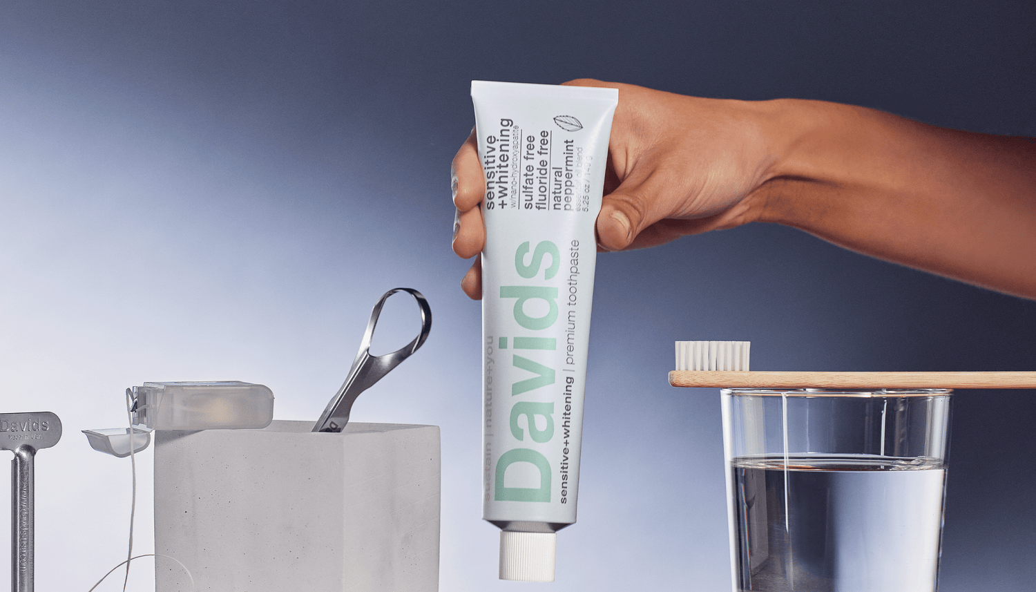 Hand holding Davids toothpaste above toothbrush and glass of water