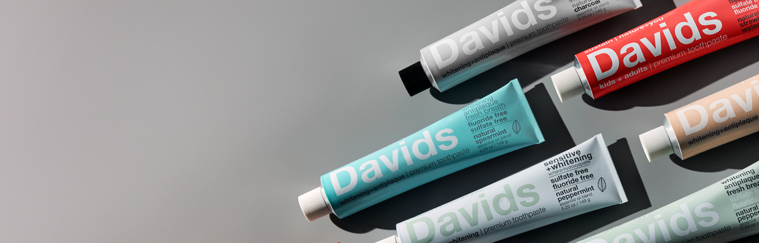 Assorted Davids toothpaste tubes in various colors arranged diagonally on a reflective surface