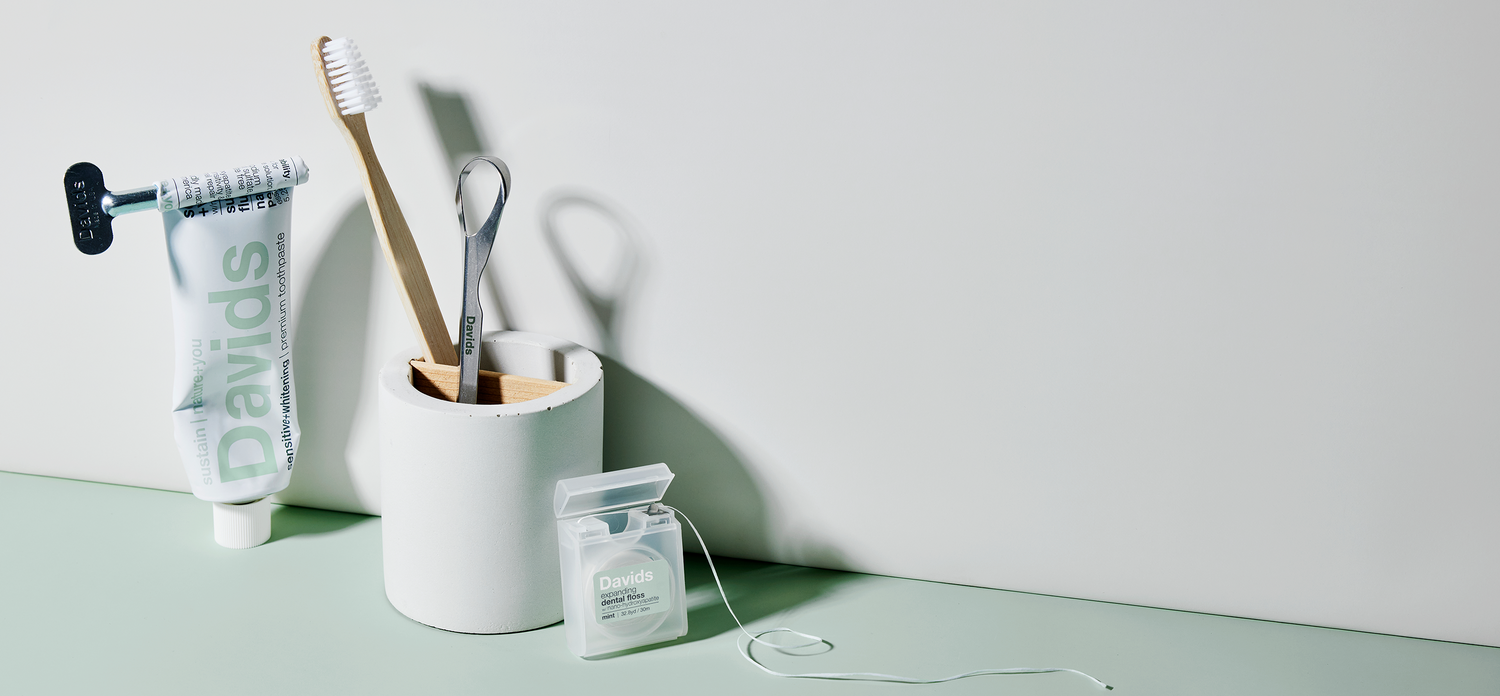 Davids toothpaste, toothbrush, tongue scraper, and dental floss arranged on a green surface