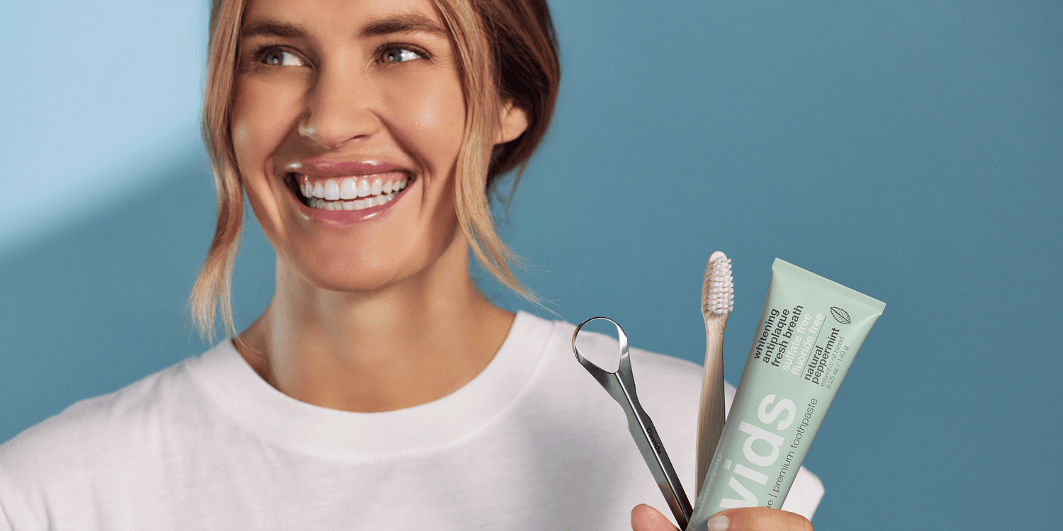 Smiling woman holding Davids toothpaste, toothbrush, and tongue scraper