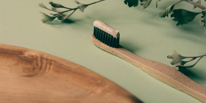 A bamboo toothbrush with natural botanicals on a green surface.