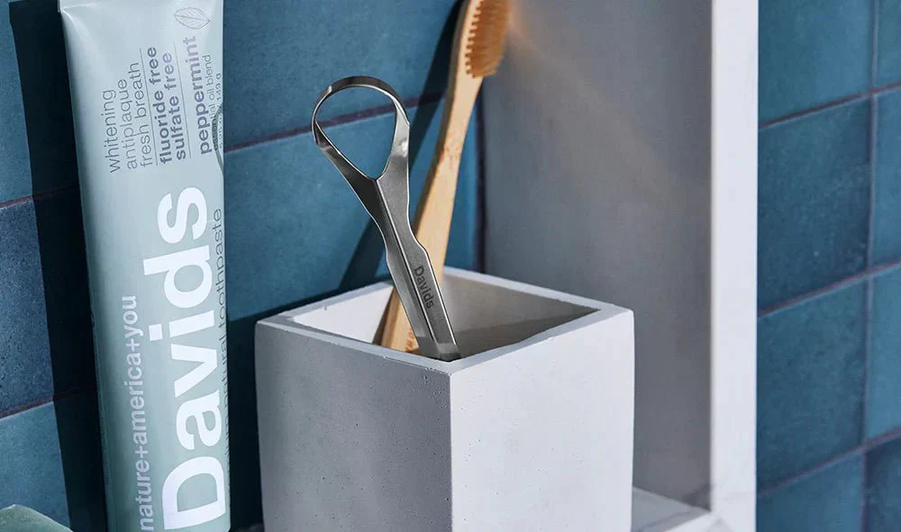 Davids tongue scraper in toothbrush holder next to Davids toothpaste