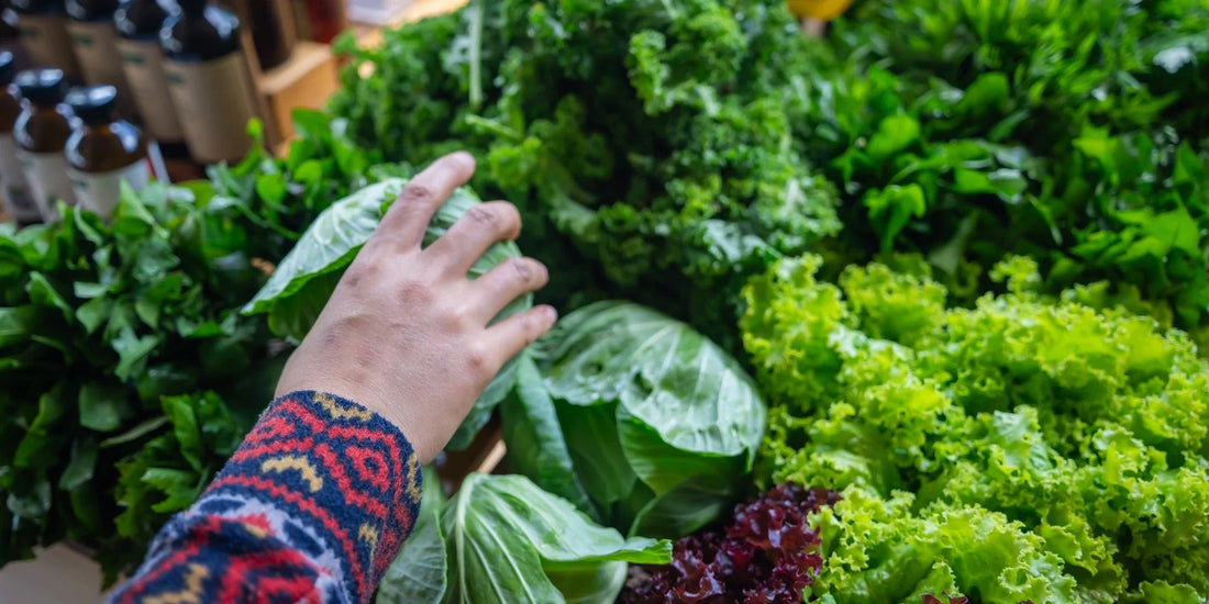 A hand picking up some kale from a vegetable display
