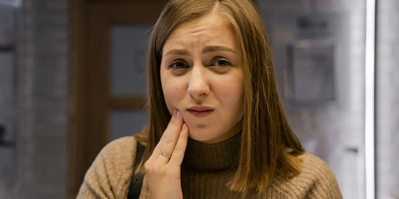 a woman with tooth sensitivity after teeth cleaning, holding her cheek in pain