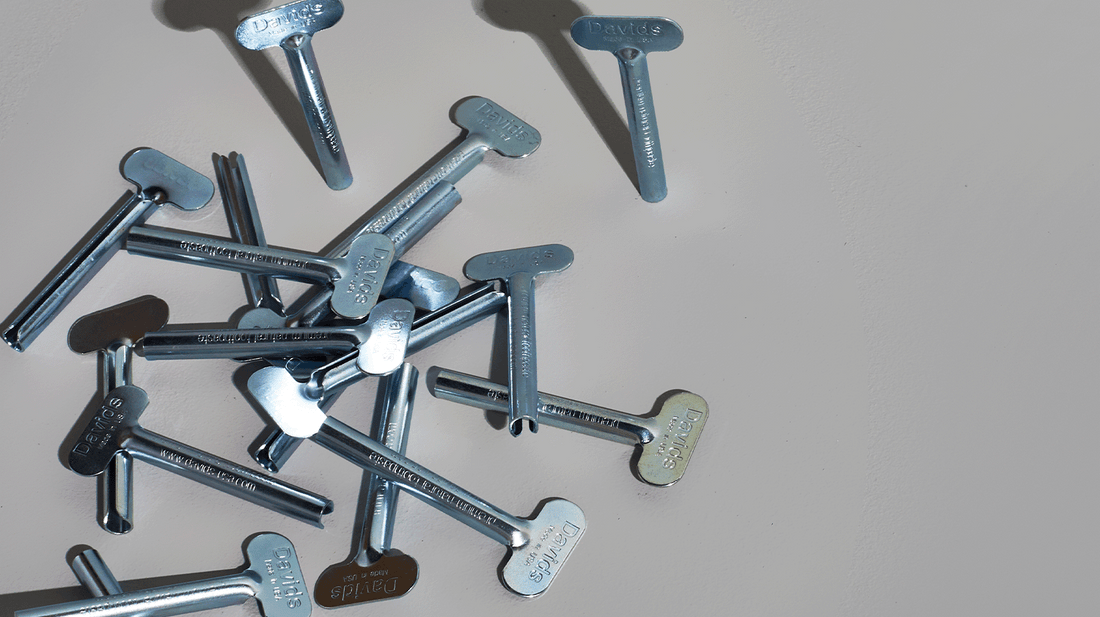 Scattered metal toothpaste tube keys labeled “Davids” on a light gray surface