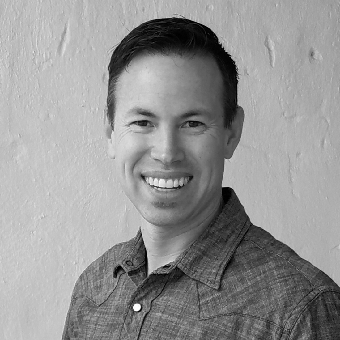 Eric Buss in a button-up shirt standing against a textured wall, shown in black and white