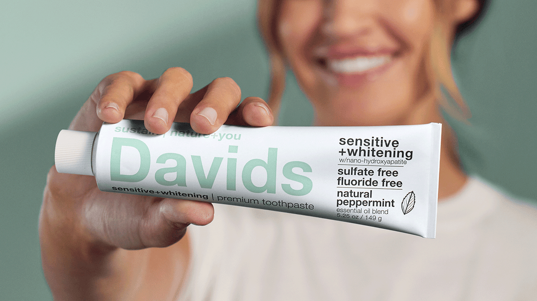 Smiling woman holding Davids sensitive+whitening toothpaste tube with natural peppermint formula