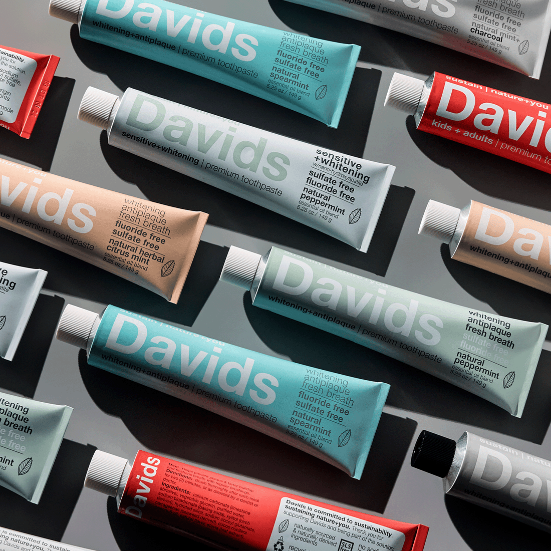 Flat lay of Davids toothpaste tubes in various colors and flavors arranged on a reflective surface